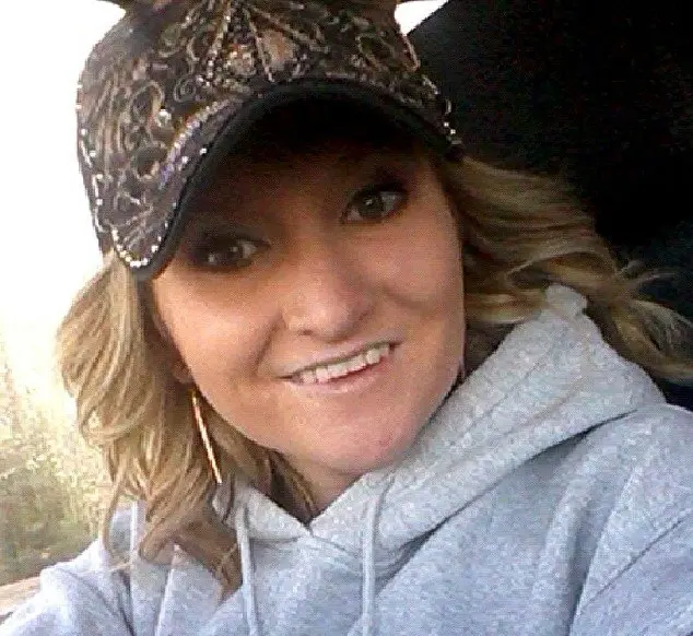 Smiling woman in a camo cap and gray hoodie.