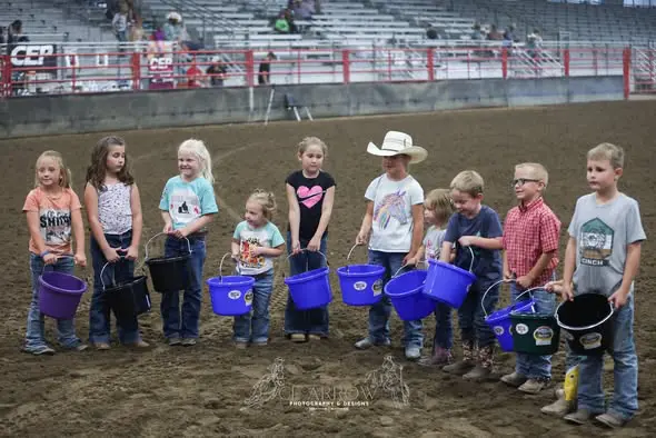 Children participating in a rodeo event with buckets and small carts.